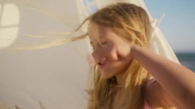 İlginç bir hikaye anlatırken küçük mutlu bir kızın portresi. Rüzgara uçan uzun sarı saçlı duygusal küçük kız. Okyanus sahilinde altın gün batımında neşeli çocuk suratı.