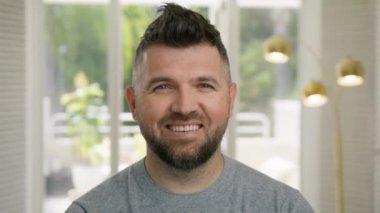Kendinden emin, yakışıklı, zeki, genç, yetişkin girişimci, lider, evde poz veren bir yönetici. Yüze yakın iş portresi 4K çekimi. Gülümseyen sakallı, olgun, profesyonel iş adamı 40 'larında kameraya bakıyor.