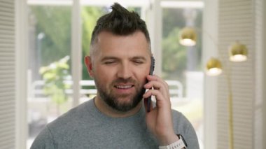 Neşeli iş adamlarının yavaş çekimde telefon almasına yakın çekim. Mutlu girişimcinin portresi. Kapalı alanda telefon açıp 4K haberlerini tartışıyor. Yakından gülümseyen 40 'lı yaşlarda cep telefonuyla konuşan bir adam.