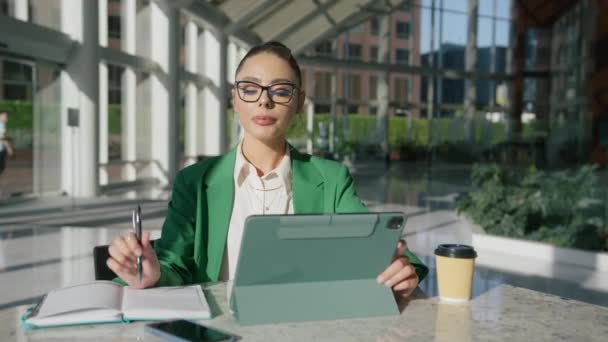 ビジネスオフィスのデジタルタブレットを使用して緑のスーツを着用するエレガントなプロのビジネス女性 都市の背景にパッド企業の技術ガジェットデバイスをタイピングするファッショナブルなビジネスウーマンエグゼクティブ — ストック動画