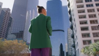 Düşük açılı kariyer insanları konsepti 4K. Günbatımında kentsel arka planda modern iş binalarında yürüyen başarılı genç ve güzel bir kadın. Çekici iş kızı Amerika 'da şirket kariyerinin tadını çıkarıyor.