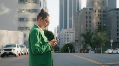 Profesyonel süitteki çekici iş kadını şehirde yürürken telefonla konuşuyor. Güzel kadın büyük şirket işvereni akıllı telefon kullanarak sokakta yalnız 4K işten sonra eğleniyor.