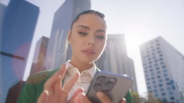 Cep telefonu kullanan kendine güvenen, modaya uygun bir kadın. Dolly 'nin yakın çekim sinematik mercek fişeği. Şehir caddesinde akıllı telefon kullanan genç ve güzel bir kadın. Arkasında güneş ışığı var.