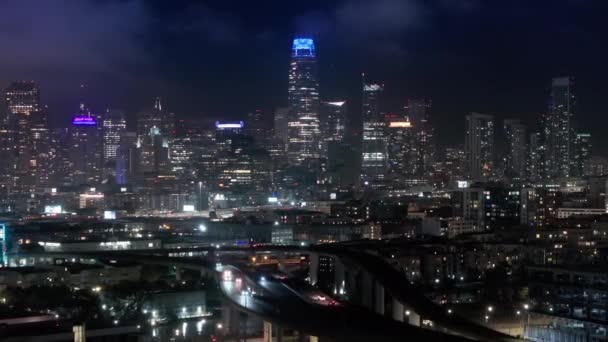 夜の照明で現代都市の景色を眺めることができます アメリカ合衆国カリフォルニア州ハイウェイを活用した交通の航空展望 夜の照明でダウンタウンサンフランシスコの夜のシネマティックパノラマ — ストック動画