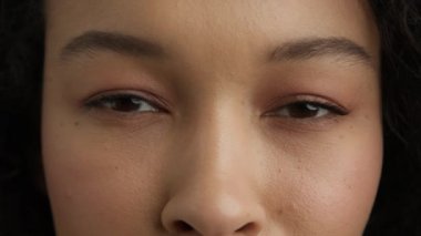 Genç ve güzel melez bir kadının siyah gözlerinden Macro shot. Yavaş çekim gülümseyen koyu kahverengi göz bebeği irisi. Moda kızı kamera 4K 'ye bakıyor. Güzel görüş, seni görüyorum. Göz bir ruhun aynasıdır.