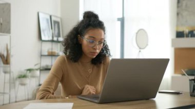 Dizüstü bilgisayarla yeni bir proje geliştiren üzgün, kıvırcık kadın girişimci endişeli. Eğitimliler 4K yavaşlar. Gözlüklü, evde bilgisayarla çalışan kafası karışık, çok ırklı, bağımsız bir kadın.