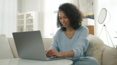 Sıradan bir kadın internette gezinirken ve oturma odasında sosyal medyada videolara bakarken eğleniyor. Güzel, stil sahibi, otantik bir kadının portresi. Ev bilgisayarında afro saç stili yazıyor.