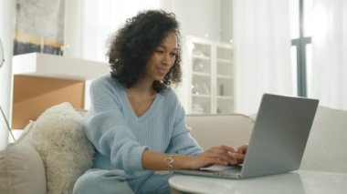 Güzel, stil sahibi, otantik bir kadının portresi. Laptop bilgisayar evinde afro saç stili yazıyor. Sıradan bir kadın internette gezinirken ve sosyal medyada oturma odasındaki videolara bakarken eğleniyor.