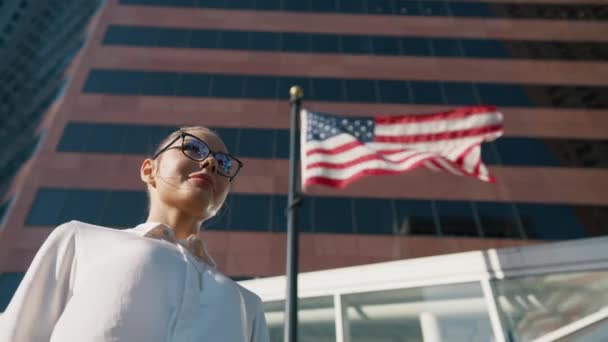 愛国的な祝日 平等な権利 民主主義 女性の権力の概念 アメリカの国旗の下に立っている誇り高い女性が風に揺れている 7月4日 独立記念日 シネマティックローアングルビュー映像 — ストック動画