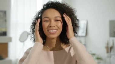 Afro saçlı güzel Afrikalı bir kızın portresi. Süslü kıvırcık saç stiline dokunuyor. Genç, dişlek, gülümseyen, dokunaklı bukleli Amerikalı kadın. Gülümseyen neşeli kız kameraya poz veriyor saçlara dokunuyor