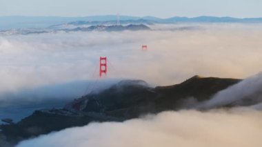 Golden Gate Köprüsü 'nün gün doğumunda San Francisco, California, ABD' de yoğun sisi delerken nefes kesen görüntüsü. Gökyüzündeki tüylü bulutları kaplayan kırmızı köprünün yukarıdan görünüşü. Seyahat konsepti, 4k görüntü 