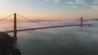Golden Gate Köprüsü 'nün San Francisco silueti, Kaliforniya, ABD' deki sabah bulutları altında görüntüsü. Güneş doğarken San Francisco Körfezi üzerinde bulunan kırmızı asma köprünün insansız hava aracı görüntüsü, 4K görüntü. 