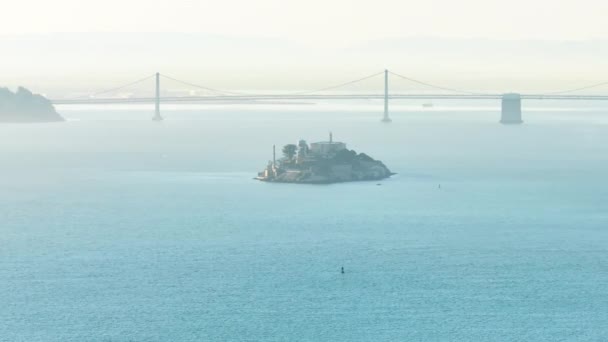 島と公園でアルカトラズ刑務所を撮影したドローン バックグラウンドの霧の中のベイブリッジ サンフランシスコ カリフォルニア アメリカ 霧の中のアルカトラズ島の連邦刑務所の航空写真 4K映像 — ストック動画