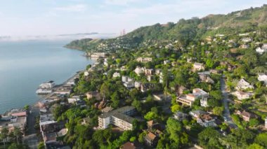 Sausalito kasabası üzerinde uçan insansız hava aracı San Francisco banliyösünde, California, batı kıyısı, ABD. Yeşil dağ tepelerindeki panoramik kasaba evleri ve villaların manzarası. Şehir simgesi, 4K görüntü