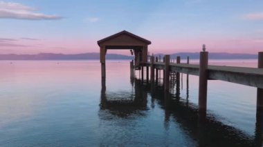 Sakin Tahoe Gölü 'nün dalgalı suları ve pastel mavisi gökyüzünü yansıtan sinematik manzarası. Dağ Gölü 'ndeki renkli bulutlu günbatımında göl kıyısındaki tekne parkında. Görüntü kopyası arkaplan 4K
