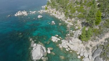 Tahoe Gölü 'nün üzerinde şeffaf turkuaz suyla uçan hava aracı. Tahoe Gölü 'nde çam ağaçları olan kayalık kıyı manzarası. Sierra Nevada dağlarına yolculuk, Nevada ABD 4K