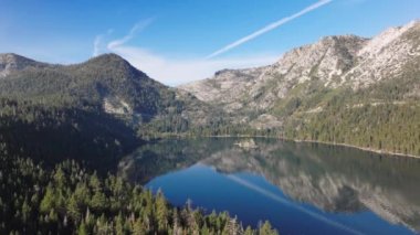 Tahoe Gölü 'nde çam ağaçları olan kayalık kıyı manzarası. Sierra Nevada dağlarına yolculuk, ABD 4K. Tahoe Gölü 'nün üzerinde uçan hava aynadaki yansıma suyu gibi.