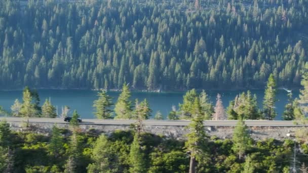 开车经过美丽的山路 公路旅行的概念 山地森林湖景汽车驶过松林 空中观光车在金色的阳光下沿着湖滨穿过松林 — 图库视频影像