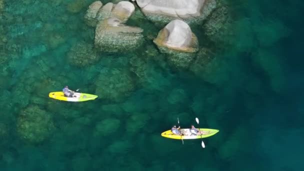 周末或假期享受大自然的人们的日常开销 场景无人机拍摄清晰透明的茶色蓝色水4K 划艇之后的空中景观 划向塔荷湖岸边的大石头 — 图库视频影像