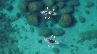 Göl yatağındaki büyük kayalıklarla şeffaf mavi suyun yukarıdan drone görüntüsü. Tahoe Gölü 'nde turkuaz sakin suyla berrak kanoda kürek çeken iki turist görülüyor.