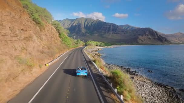 夏休みのアドベンチャーツアー オアフ島の火山に向かって劇的な岩の海岸沿いの沿岸道路で運転する空中ビューブルーコンバーチブルカー ハワイを旅行する幸せな若いカップル — ストック動画