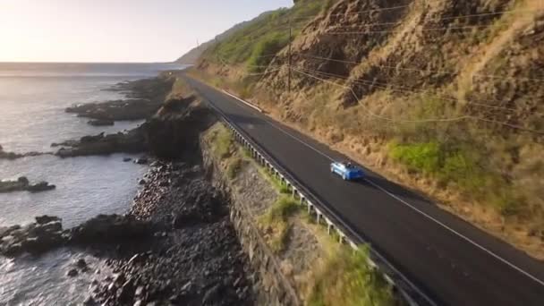 山道で青いスポーツカーに乗る空想的な幸せな観光客 ジョイ未来のアウトドアアドベンチャー 晴れたクリーンロードハイウェイ島で運転するドローン高価なブルーラグジュアリーコンバーチブルバケーションカー — ストック動画