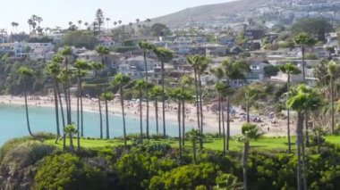 Panoramik tatil köyü manzarası - Laguna plajı çarpıcı okyanus manzaralı, Orange County, California, ABD. İnsanlar plajda takılıyor. Pasifik Okyanusu 'ndaki yüksek palmiye ağaçları ve dağlarıyla manzara