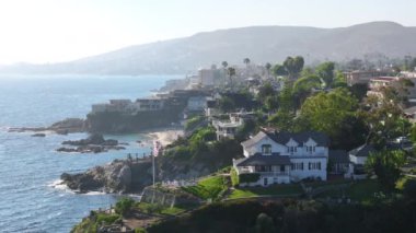 Orange County, Kaliforniya 'daki Laguna sahil şeridine kuşbakışı bakış açısı. Pasifik Okyanusu 'ndaki sahil beldesi. Dağlık manzaralı evler. Rüzgarla dalgalanan Amerikan bayrağı