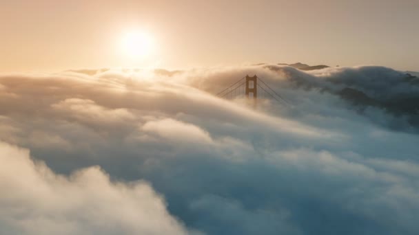 サンフランシスコ カリフォルニア州ゴールデンゲートブリッジ周辺を飛行する厚い雲 赤い橋4Kを覆う景色のティールオレンジの濃い霧 映画的な雲の景色で日光が輝く美しい黄金の日没 — ストック動画