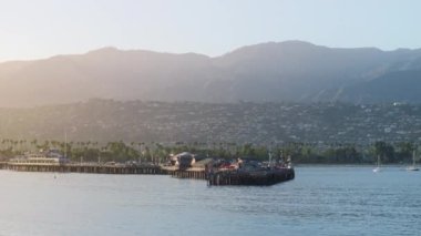 Stearns Wharf 'ın ve Santa Barbara' nın günbatımında, Kaliforniya, ABD 'de şehir manzarasının uzaktan çekimi. Şehir limanının yelkenli yatlı insansız hava aracı görüntüsü. Pasifik Okyanusu 'nun su yüzeyine düşen güneş ışığı, 4k görüntü 
