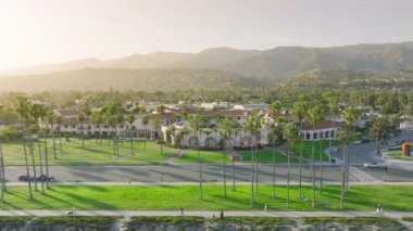 Santa Barbara 'nın günbatımındaki manzarasının panoramik görüntüsü, Kaliforniya, ABD. Resort City 'nin arka planında dağlar olan gökyüzü görüntüsü. İnsanlar deniz kenarında yürümekten zevk alıyor, 4K görüntüler. 