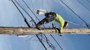 CALIFORNIA, ABD-30 Ekim 2023: elektrik direğine tırmanan elektrikçi. Üniformalı ve kasklı bir erkek işçi. Tamircinin şebeke hattını tamir ederken dikey çekim. Tehlikeli işi olan bir mühendis. 