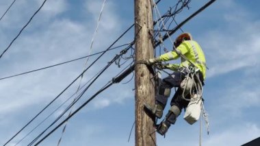 CALIFORNIA, ABD-30 ECTOBER 2023: tehlikeli bir işi olan elektrik mühendisi emniyet kemeri ile direğe tırmanıyor. Erkek elektrikçi elektrik direğindeki yüksek voltaj kablolarını kuruyor ve onarıyor