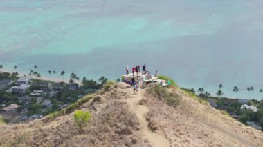 İnsanlar Hawaii 'deki Pillbox Patikası' nın tepesindeki Lanikai plajının sinematik manzarasının keyfini çıkarıyorlar. Hawaii Oahu Adası 'ndaki Kaiwa Ridge Patikası' nın tepesinde maceraperest turistler. Açık hava macera konsepti 4K