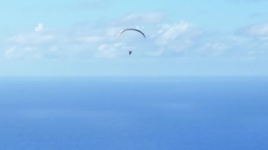 Havada, Pasifik Okyanusu üzerinde, Hawaii ABD 'de paraşütçü pilotsuz hava aracı görüntüsü. Açık mavi gökyüzünde beyaz bulutlarla uçan olağanüstü bir paraglider. Adam gökyüzünde 4K paraşütle uçuyor.