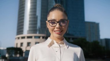 Modern ofis binasında arka planda poz veren şık gözlükler takan parlak saçlı, gülen yüzlü genç yetişkin bir kız. Kafasından vurulmuş. 4K portresi yakın plan.