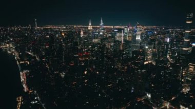 Karanlık çöktükten sonra gökdelenlerin üzerinde İHA uçuşu. Gece vakti modern gece şehrinin üzerinde. Aydınlanmış Manhattan USA. New York şehrinin arka planı. Şehir merkezindeki Hava Saati Meydanı