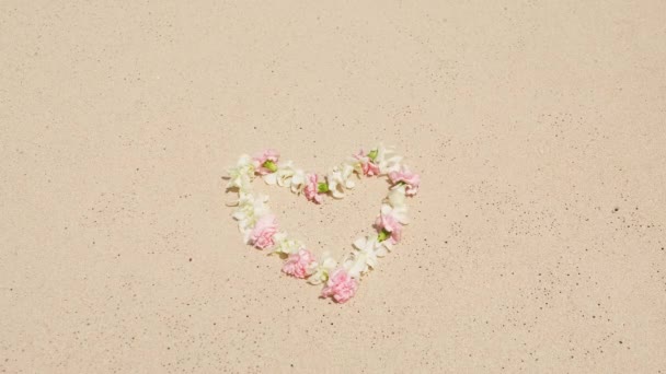 白とピンクの熱帯フラワーレイ 暖かい海の泡立った波によって洗浄された心の形 愛のコンセプト セントバレンタインデー 結婚式の日の背景 砂浜に横たわる花の心の形の愛のシンボル — ストック動画
