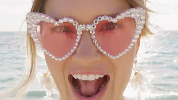 以心形的迷人的粉色眼镜把漂亮女人的画像合拢起来 非常积极的金发女士 开朗的笑容和洁白的牙齿到处鬼混 情人节快乐 情人节惊喜 — 图库视频影像