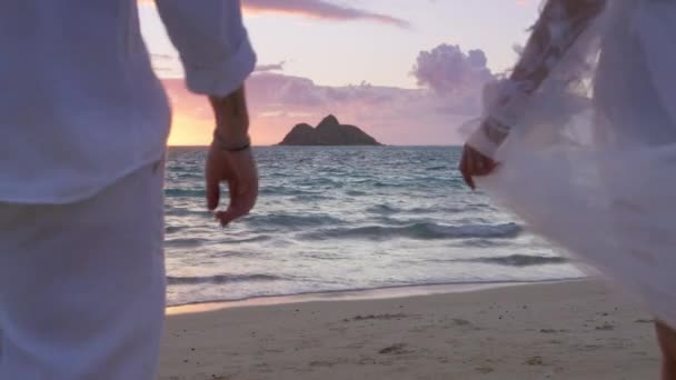 在户外的婚礼上 穿着飘飘欲仙的婚纱和新郎一起靠岸的美丽新娘的背影 在日出时分 新婚夫妇在美丽的海滩上缓缓走向私奔 — 图库视频影像