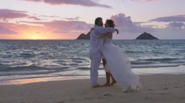 Yeni evli çiftimiz yaz günbatımında tropik plajda birbirlerine sarılıyorlar. Boho tarzı düğün kıyafeti giymiş romantik bir çift birlikte dışarıda romantik bir hayat sürmekten hoşlanıyor. Aşk konsepti 4K