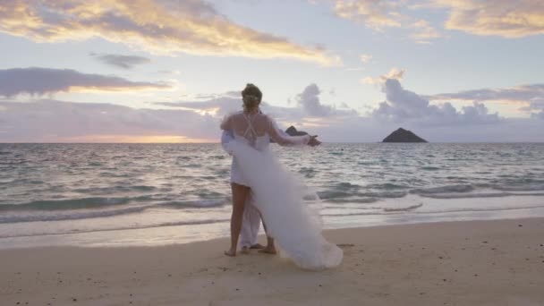 浪漫快乐的拥抱年轻夫妇分享美丽的第一个婚礼舞蹈时刻在夏威夷海滩日落 恋爱中的伴侣享受着私奔的海滩仪式 无忧无虑的爱人们在海滩上跳舞 — 图库视频影像
