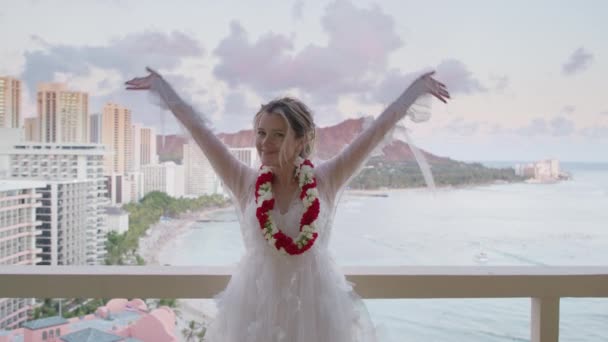 年轻快乐的女人张开双臂站在度假村的阳台上 穿着红莱茵项链的笑容满面的新娘享受着夏威夷蜜月之旅4K 夏威夷落日 怀基基海滩尽收眼底 — 图库视频影像
