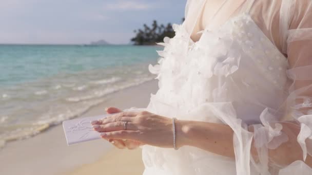 花瓶の本を持っている女性の手のクローズアップショット エループの背景 美しい白い花のブーフウェディングドレスで認識できない花嫁は ビーチの結婚式で成長することを誓います — ストック動画