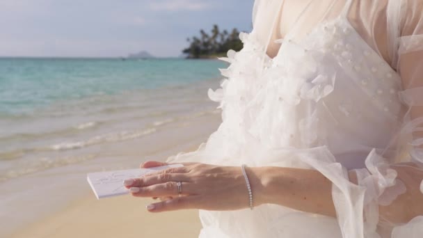 美しい白い花のブーフのウェディングドレスで認識できない花嫁は ビーチの結婚式で成長することを誓います 花瓶の本を持っている女性の手のクローズアップショット エロペーションの背景 — ストック動画