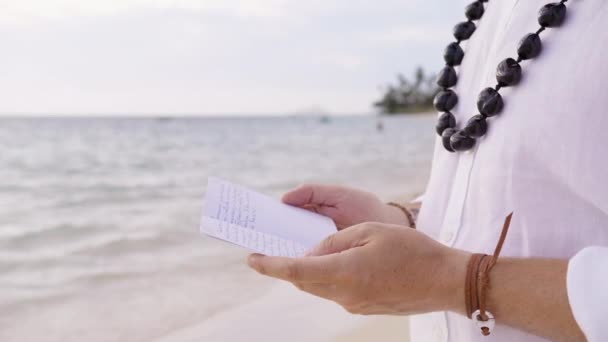 海滩婚礼背景与特写镜头男性的手宣读他的誓言仪式 夏威夷热带岛屿上身穿白色亚麻布衬衫 戴着传统的Kukui坚果项链 并有一本公开的誓言书 — 图库视频影像