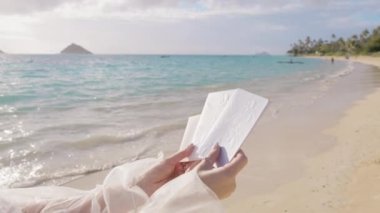 Gelin, evlilik yeminini romantik duygusal yeminlerle ve tropik plajda el yazısıyla yazılmış kelimelerle açar. Kutlama geçmişine bayılırım. Beyaz çiçekli bir gelinlik içinde elinde kabartmalı kitaplar tutan bir kadın.