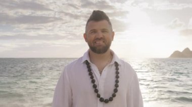 Hawaii adalarında geleneksel kukui fındık kolyeli, boho düğün kıyafetli yakışıklı bir erkek. Kumsalda kameraya bakan yakışıklı bir adam. Beyaz keten gömlekli ve şık saçlı gülen damat portresi.