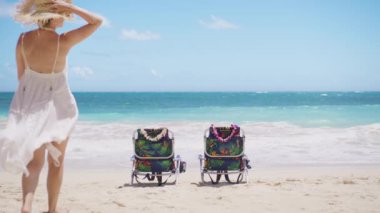 Beyaz uçan boho elbiseli kadın yaz tatilinin tadını çıkarıyor. Plaj sandalyelerinde dinlenen bir kadın. Cennet tropik ada arka planı. Oahu, Hawaii adasında deniz mavisi okyanusla birlikte sinematik seyahat.