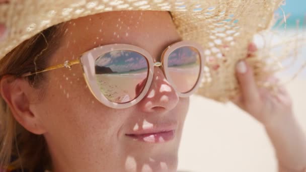 ストロー帽子の若い日差しの女性の近くの顔は 鏡のサングラスを反映した海のビーチを見ます 美しい女性の肖像画の笑顔は 夏休みにハッピーアウトドアを感じます スローモーショントラベル — ストック動画
